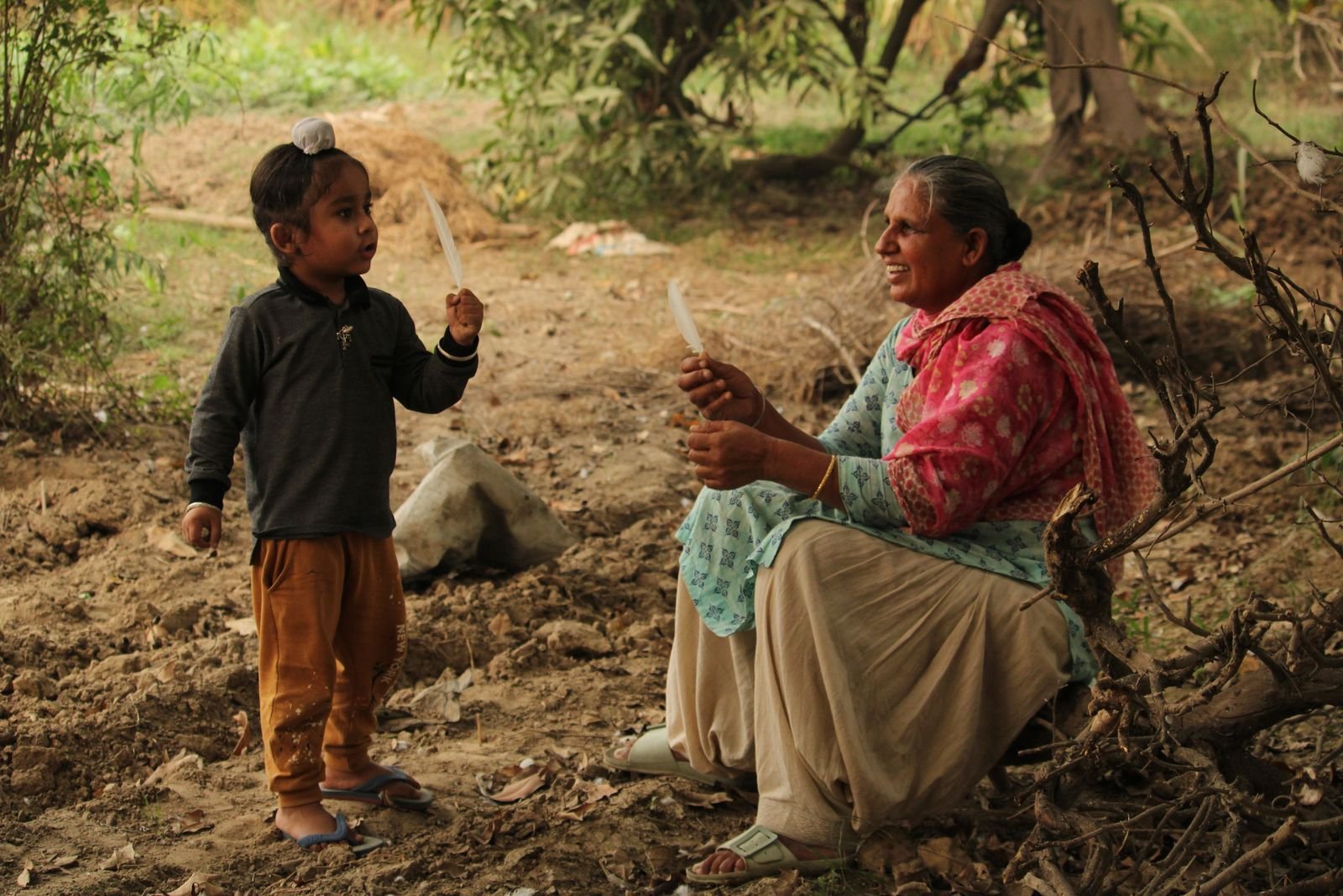 A grandmother laughing with a young grandchild outdoors in a village in India