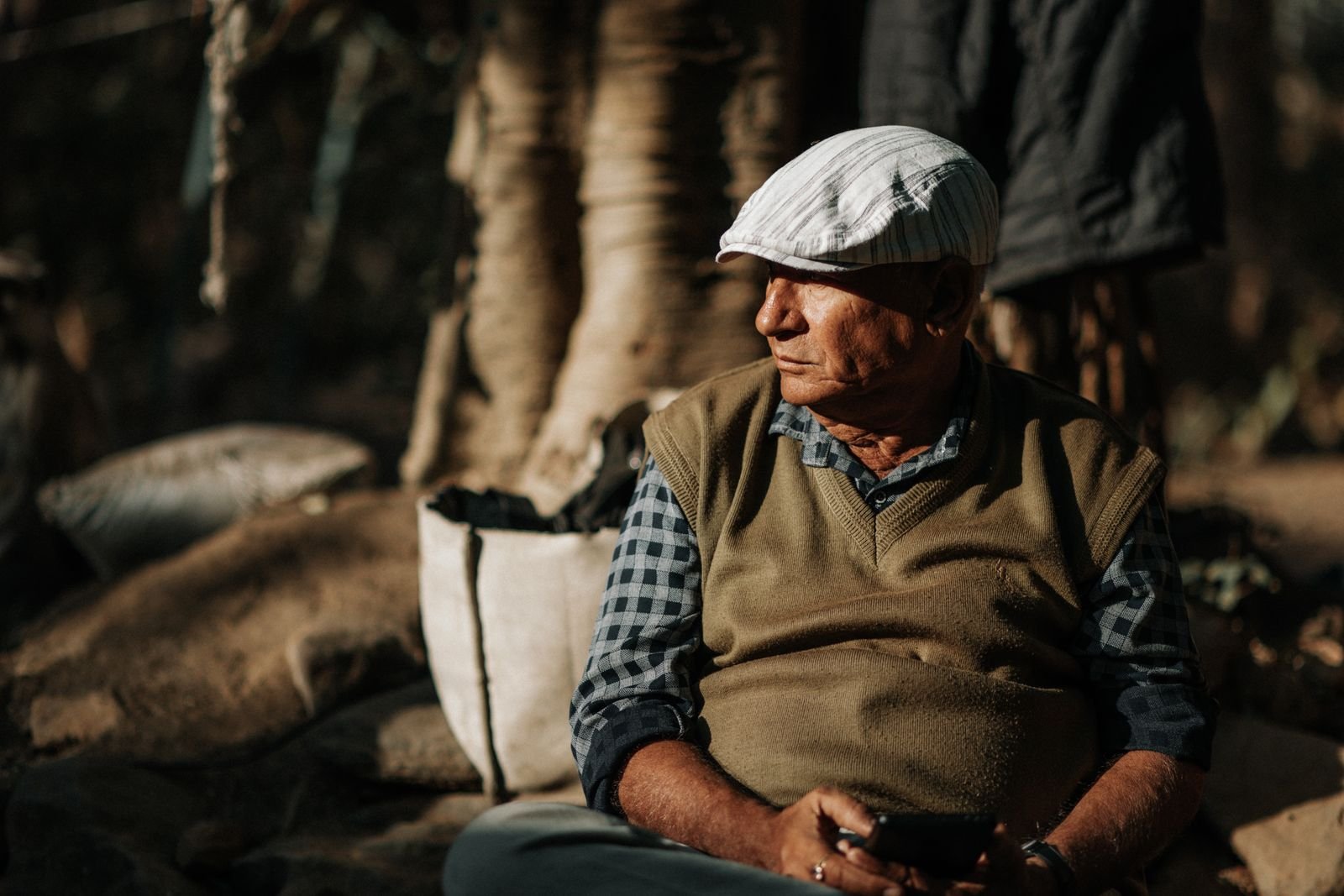 An older man in a cap sitting in the sun with a smartphone in his hand